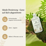Eine Frau hält eine Flasche Vita Shield Plus+ Immunshots von Golden Elements, mit einer natürlichen Landschaft im Hintergrund.